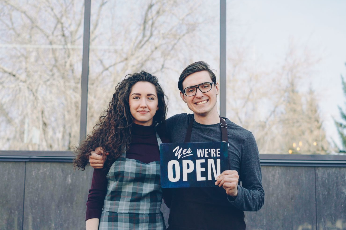 Independent shop owners holding an open sign at their storefront